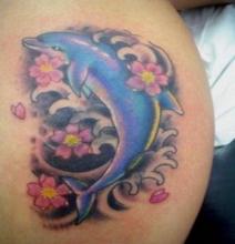 Цветная тату в виде дельфина с цветами на плече