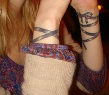 Цветная татуировка на запястьях девушки - браслет в виде ленты с бантом